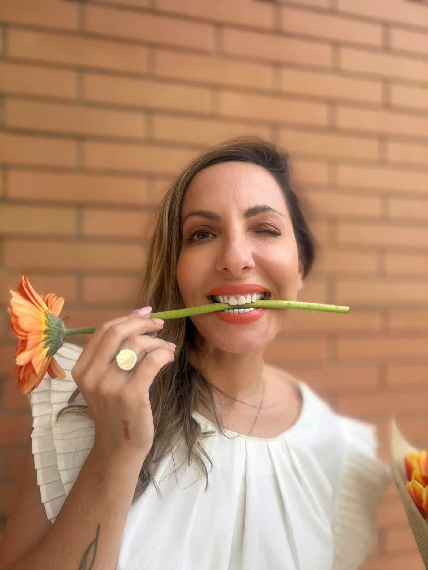 Sophia Georgopoulou with a flower between her teeth, against a brick wall